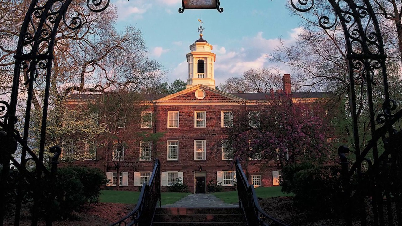 Rutgers' Old Queens building, with a white cupola, framed by a dark, ornate wrought iron archway.